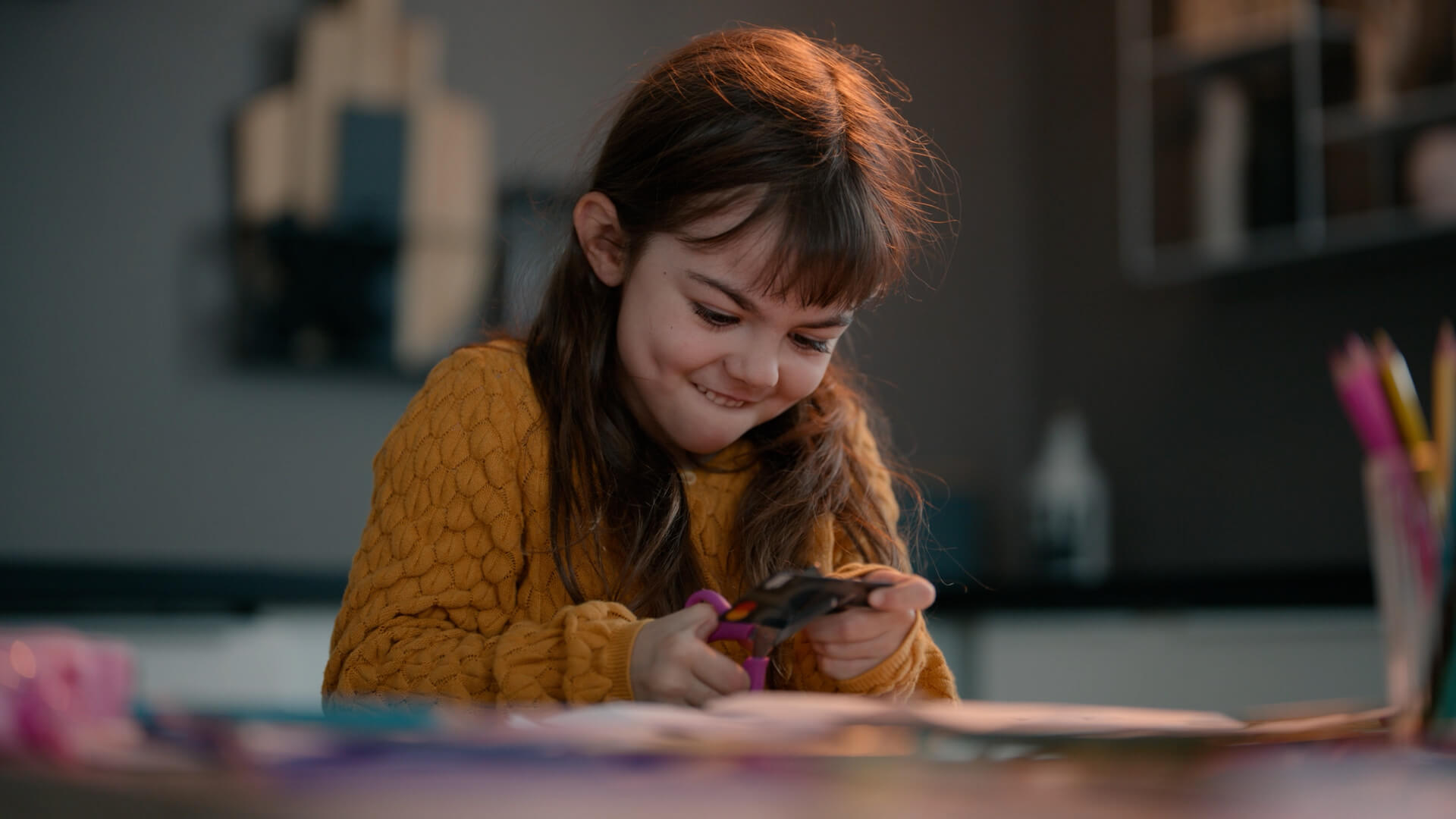 Lite barn i gul genser klipper opp et bankkort med en saks, med et rampete smil, ved et bord fullt av fargerike tegnesaker. Fra en reklamefilm laget av Headspin