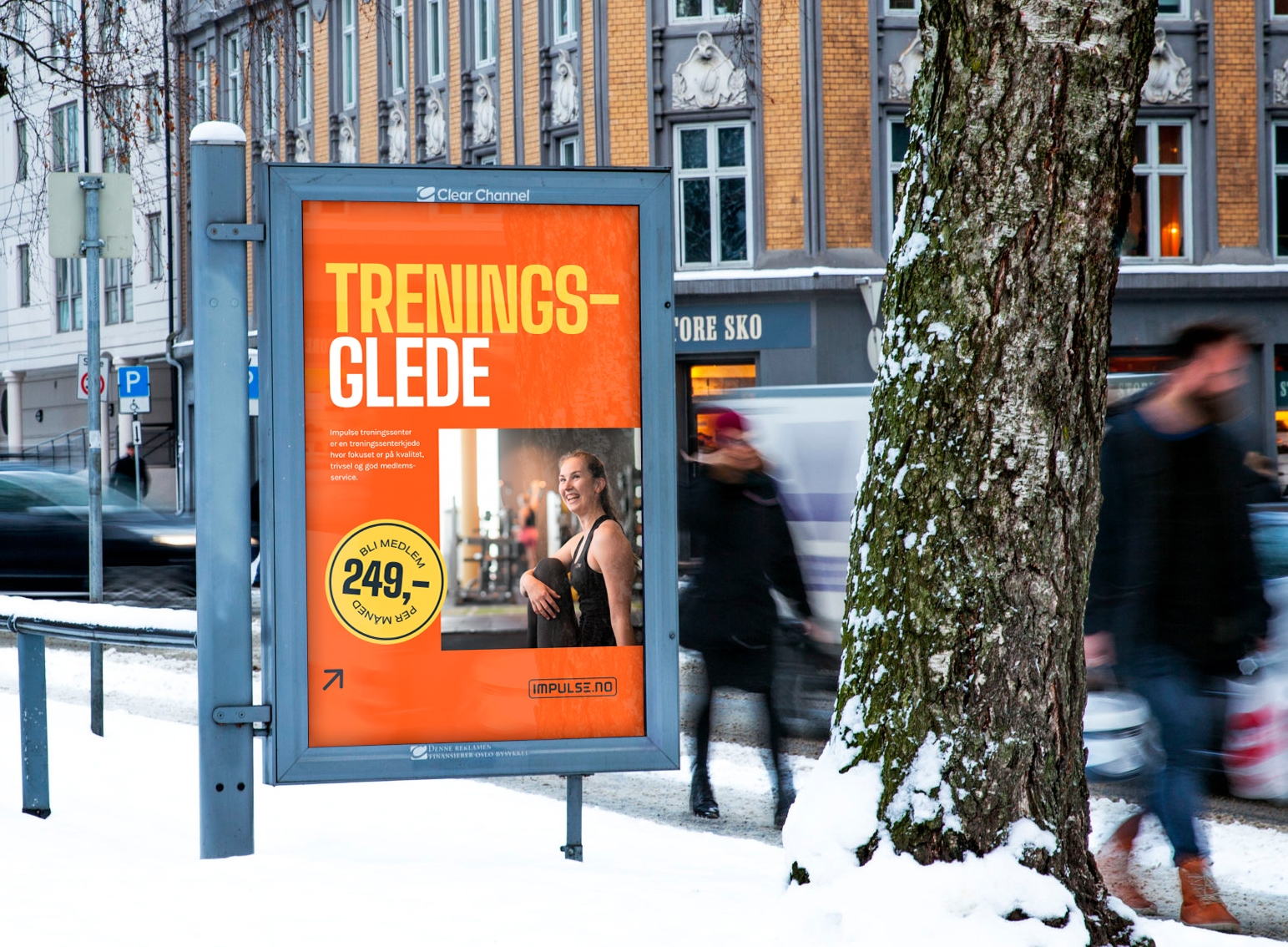Visuell plakatdesign for reklamekampanje – moderne digital plakat for Impulse Treningssenter med bilde av kvinne og budskapet «Treningsglede», vist i bygate om vinteren